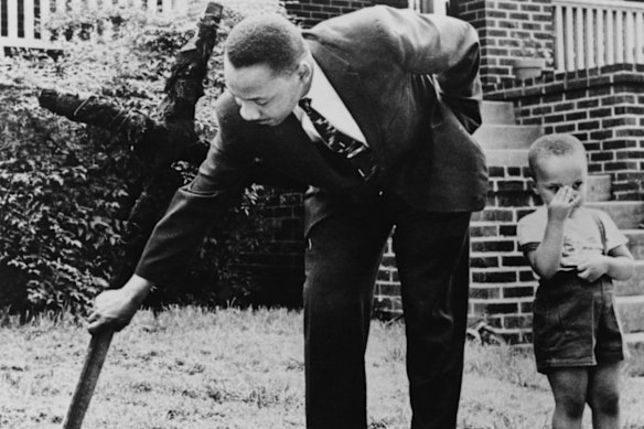 Martin Luther King III as a toddler with his father, who is removing a burnt Ku Klux Klan cross from the front lawn of their home in Atlanta, 1960.
