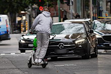 A man rides an E scooter the wrong way down Little Bourke with no helmet, swerving to miss an oncoming car.