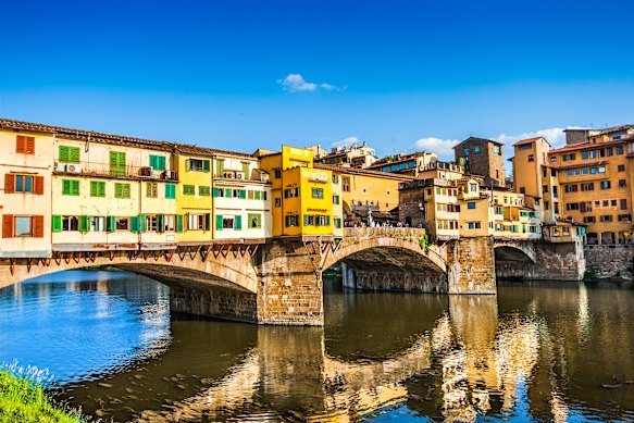 Reflections from the medieval Ponte Vecchio extend across the Arno river in Florence, Italy.