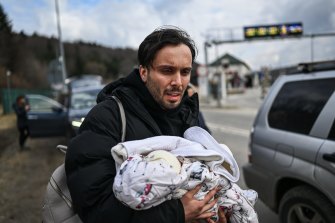 Un homme porte son bébé d'un mois alors qu'il arrive en Pologne après avoir traversé la frontière à Kroscienko dimanche.