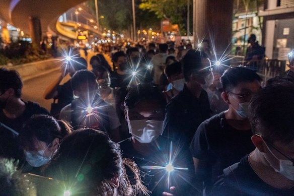 People hold up their phones with the light on as they walk near Victoria Park on June 4, 2021.