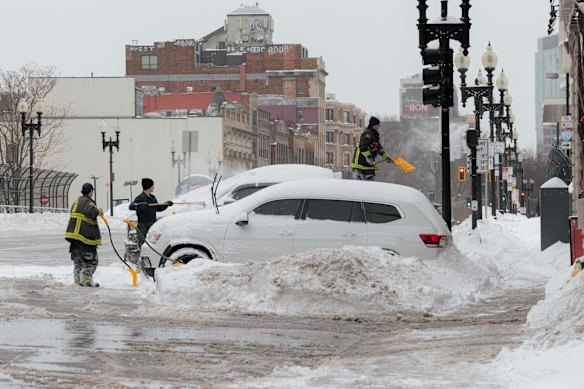 Firefighters clear snow from vehicles in Boston, Massachusetts.
