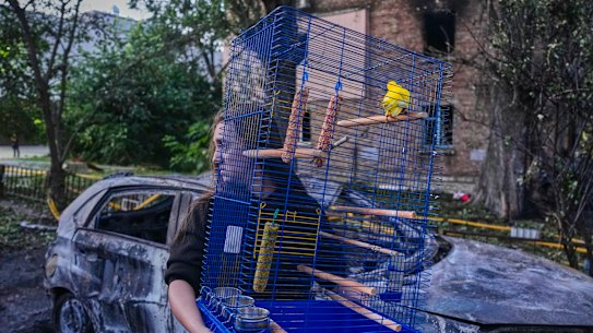 A woman carries a cage with a parrot as she leaves her damaged house following a Russia missile attack in Kyiv.