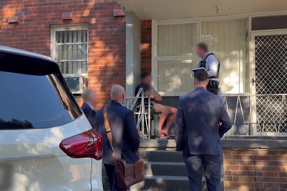 A man speaks with police and disability insurance fraud investigators during a raid on a Villawood home in December.