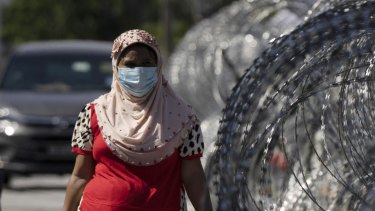 一名妇女带着杂货回家，在马来西亚吉隆坡的Selayang Baru的冠状病毒封锁区域的铁丝网旁边。