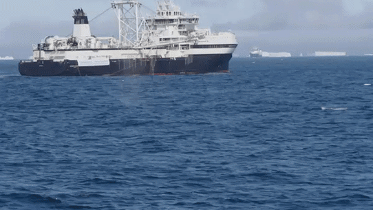 A whale breaches in the Antarctic near a krill trawler.