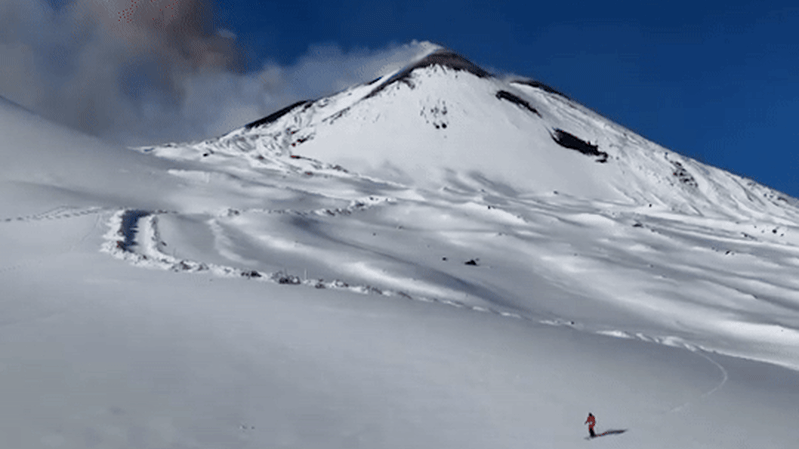 Skier glides down Mount Etna as volcano erupts in the background