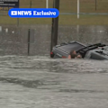 An ABC reporter and a stranger have rescued a man whose car was sinking in floodwater near Brisbane.