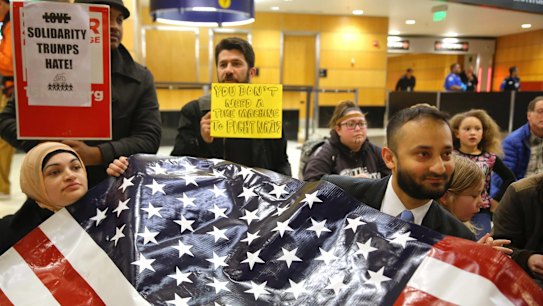Sabrina Sheikh, left, a naturalised citizen who immigrated to the US from Pakistan at age two, and Arsalan Bukhari, right, hold up a flag that reads "We are America" in Seattle.