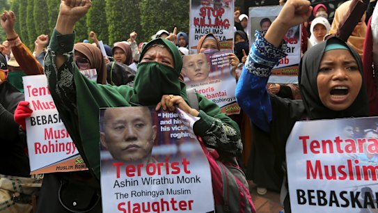 Muslim women, holding a poster depicting Wirathu, the leader of Myanmar's nationalist Buddhist monks, raise their fists outside Myanmar Embassy in Jakarta, Indonesia.