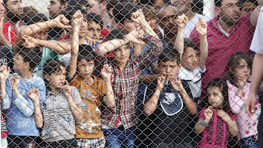 Migrants stand behind a fence at the Nizip refugee camp in Turkey.