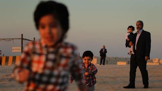 Khalid Mishal (right), leader of Hamas, holding his one year old granddaughter Sara (2nd from right) whilst going for a walk with his grandsons  Bara 4yrs (left) and Saad 2yrs (2nd from left) in the suburban streets of Doha, Qatar. A bodyguard provides security in the distance (3rd from left). 6th February, 2013. Photo: Kate Geraghty