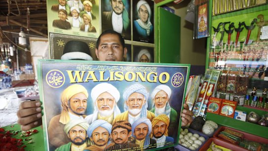 A vendor of merchandise at the shrine with a poster of the Wali Songo, or nine saints, credited with bringing Islam to Java.