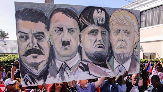 I membri della comunità haitiana tengono un cartello raffigurante le immagini, da sinistra, di Joseph Stalin, Adolf Hitler, Benito Mussolini e Donald Trump durante una protesta vicino alla tenuta di Trump a Mar-a-Lago lunedì.