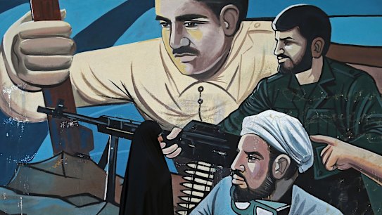 A woman walks past of a mural depicting members of Iran's Basij volunteer paramilitary force, on a quiet street in downtown Tehran.