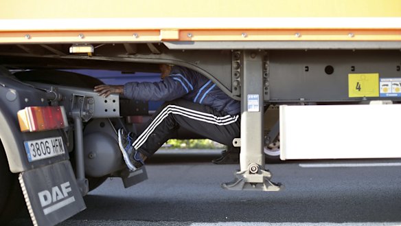 A migrant sits under the trailer of a lorry as he attempts to cross the English Channel, in Calais, northern France on Wednesday.