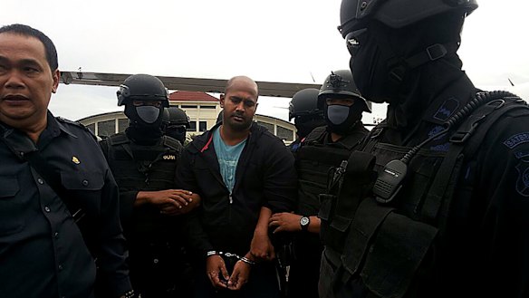Myuran Sukumaran is surrounded by masked security personnel upon arriving at Cilacap airport.