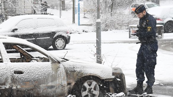 A policeman investigates a burnt-out car in Rinkeby outside Stockholm after the riot.