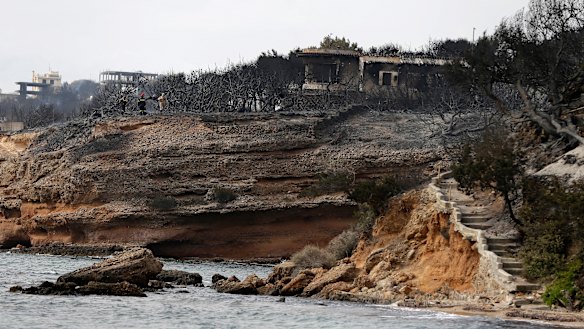 Firefighters stand on a cliff top where burned trees hug the coastline in Mati east of Athens, Tuesday.