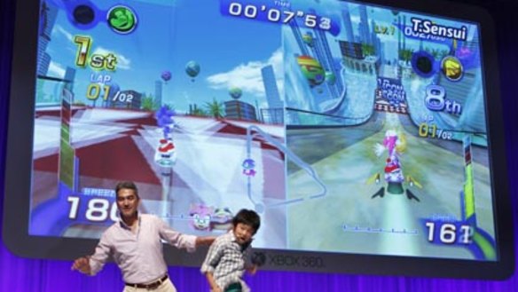 Microsoft Japan's Home & Entertainment General Manager Takashi Sensui, left, and a model boy demonstrate Microsoft's Kinect motion-sensing system.