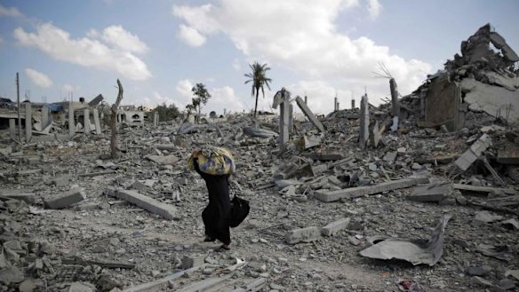 A Palestinian woman carries belongings from the remains of Khuza'a.