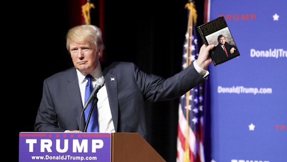 Donald Trump holds up a copy of his 1987 book, Trump: The Art of the Deal. 