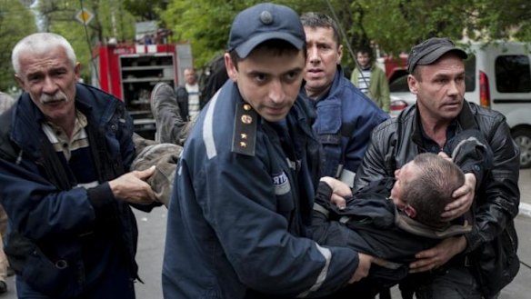 Police and citizens carry a firefighter injured during an attack on a police station in Mariupol, eastern Ukraine.