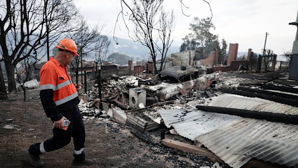 An electricity worker inspects properties on Wildlife Drive in Tathra after the bushfire.