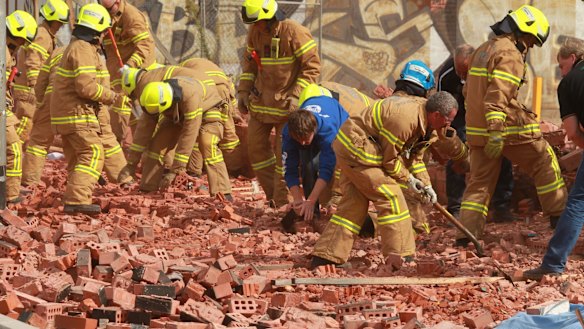 Firemen and workers with bare hands frantically dig into the fallen brick wall in Swanston Street in 2013.