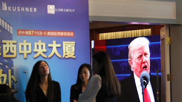 A projector screen shows footage of US President Donald Trump as workers wait for investors at a reception desk during an event promoting a Kushner Companies development, in Shanghai, China, on Sunday.