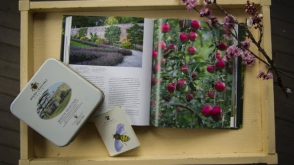 A copy of <i>Highgrove: A Garden Celebrated</i>, some fruit blossom, a tin of Duchy Originals biscuits, and a pack of Highgrove bumblebee cards, photographed on the front verandah at Calthorpes' House.