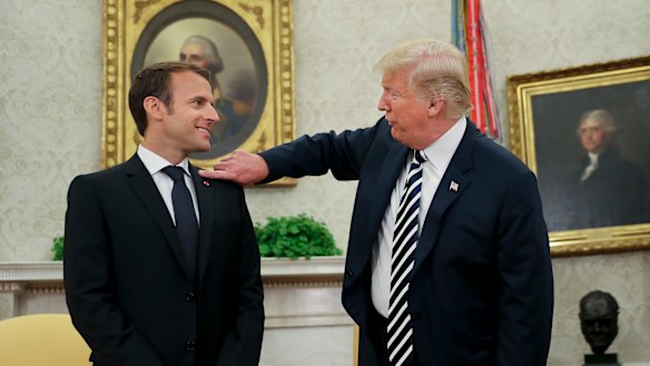 President Donald Trump playfully reaches over to clean "dandruff" or lint off French President Emmanuel Macron.