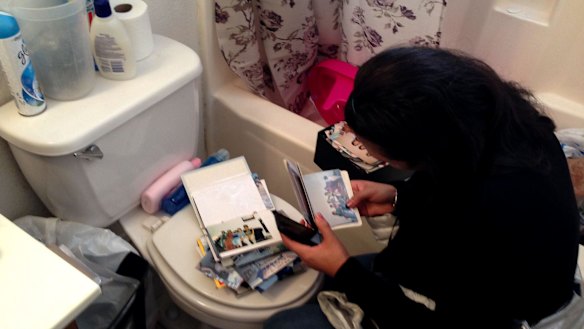 A woman straddles the toilet and rifles through photo albums.