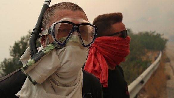 People cover their faces from the smoke that fills the sky near Kineta, west of Athens, after roads were blocked due to forest fires on Monday.