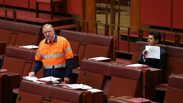 Liberal Senator Ian Macdonald speaks on the mining tax repeal while Scott Ludlam holds up a sign. Photo: Alex Ellinghausen