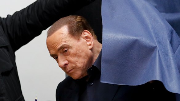 Italian former premier and leader of Forza Italia party Silvio Berlusconi holds his ballot as he is helped get out of a polling booth, in Milan.