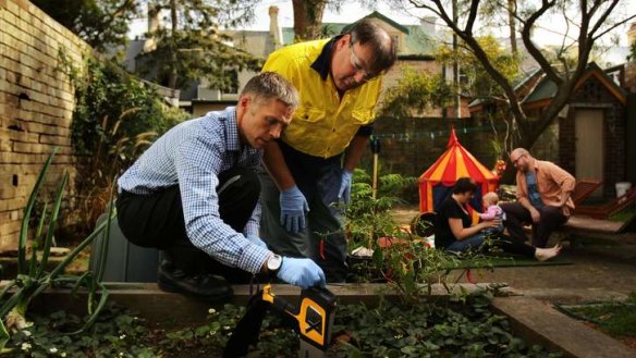 Dirty bomb: Mark Taylor and Damian Gore test the soil in the backyard of Tilly Boleyn and Rick Calder (in background with infant daughter Saskia) for lead levels.