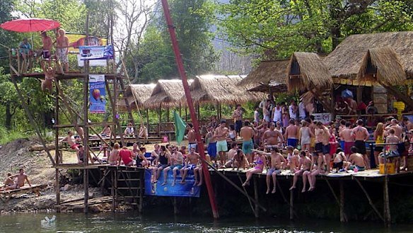 Tourists crowd a riverside bar, by one of the towers used for leaping into the river.