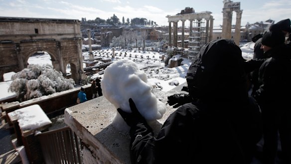 Sculptor Francesca Antonello moulds snow into a face as people look out towards the ancient Roman Forum covered in white.
