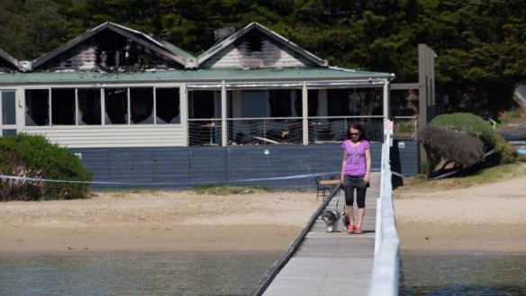 A woman walks her dog on the pier in front of "The Baths", the morning after fire gutted the popular function and wedding centre.