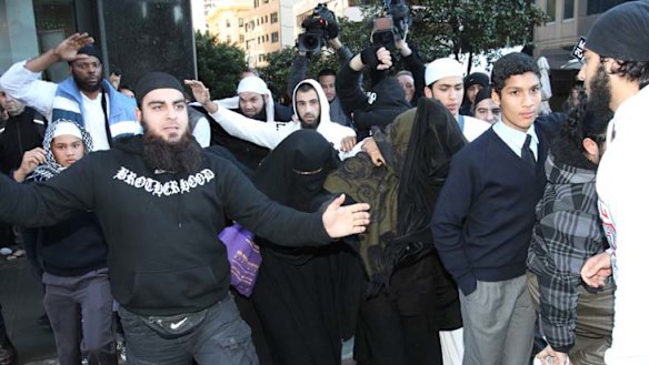 Carnita Matthews, covered centre, is shielded by a group of men yesterday.