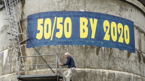 Matthew Nott, president of the Clean Energy For Eternity group, stands next to a sign that he painted on the Tathra Water tower, in 2016.