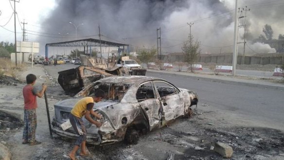 Children stand next to a burnt-out car during clashes between Iraqi forces and insurgents in the northern Iraqi city of Mosul.