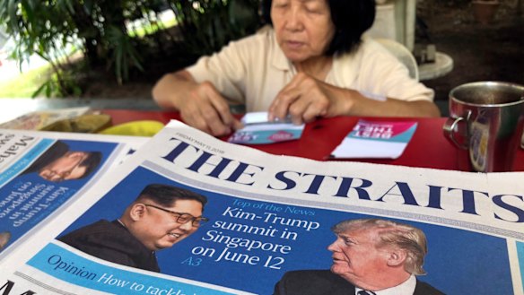 A news vendor counts her money near a stack of newspapers with a photo of Trump, right, and Kim on its front page in Singapore. 