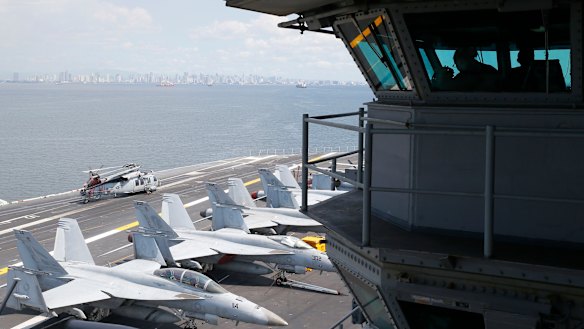 US Navy officers operate on the flight deck control tower as military aircraft sit on the flight deck of the USS Carl Vinson.