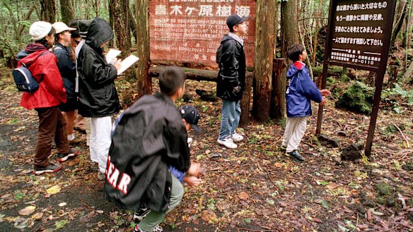A group of schoolchildren read signs posted in the dense woods of the Aokigahara Forest at the base of Mount Fuji.