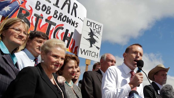 Protesters hold up controversial posters behind Tony Abbott as the Opposition Leader   speaks at the No Carbon Tax rally outside Parliament House in Canberra.