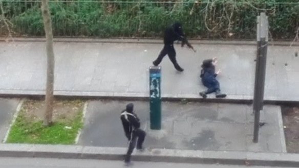 A hooded gunmen stands over a wounded police officer before executing him at point-blank range in this still from an amateur video capturing the terrorist attack.