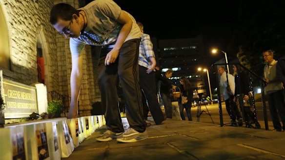 Jonathan Neighbors, 15, adds light to one of the 59 luminaries set on the front steps of Greene Memorial United Methodist Church for victims of the shooting 