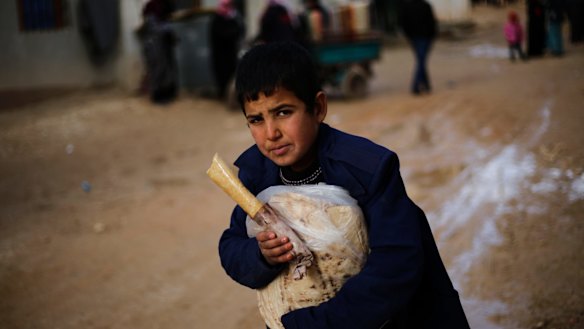 A Syrian boy displaced from eastern Aleppo holds a sandwich and bread bag in the village of Jibreen on Saturday.